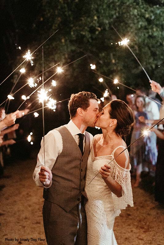 Bride and groom kissing under the sparkler send off, while holding sparklers