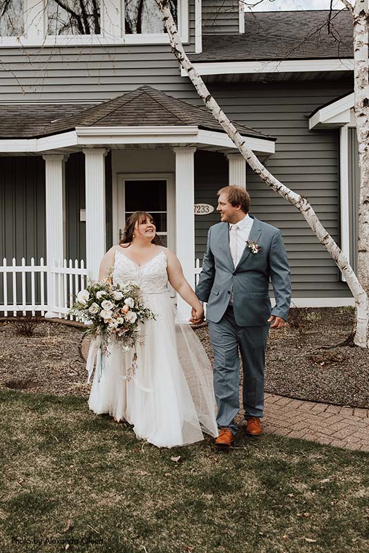 Groom in blue suit and bride in blush dress walk out of house