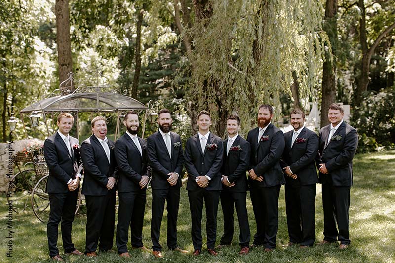 Groomsmen and groom in navy suits stand outside