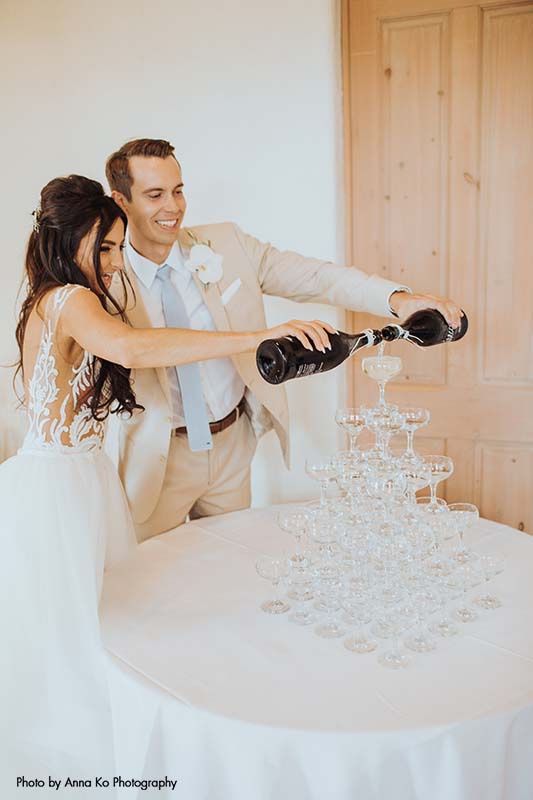 Bride and groom pour champagne into glass tower