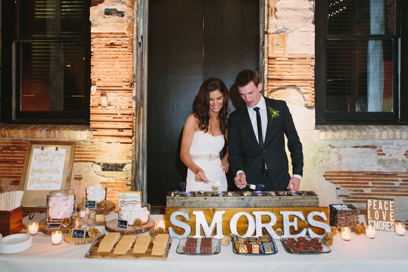 Bride and groom roast marshmallows over fire at s'mores bar by North mallow