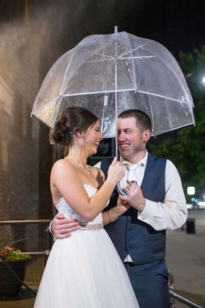 Bride and groom stand under umbrella