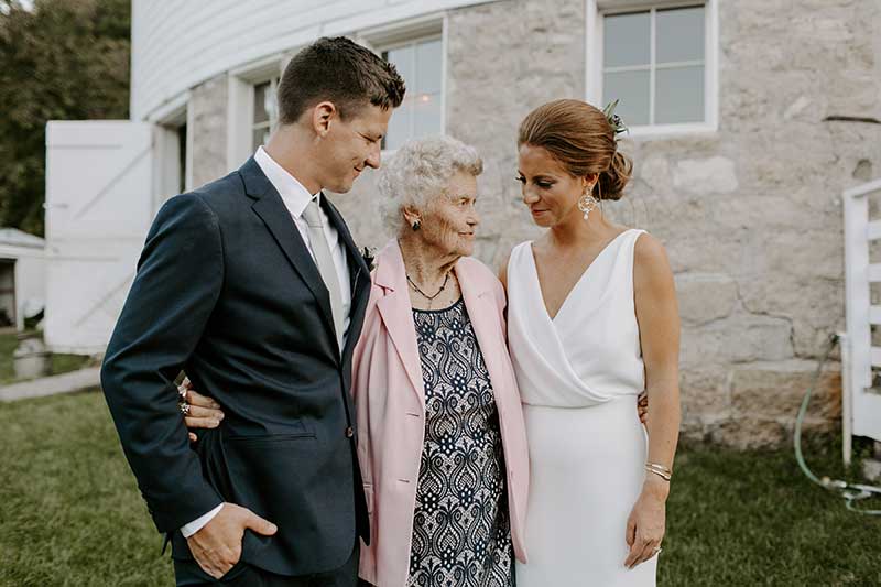 Bride and groom stand with grandmother at wedding