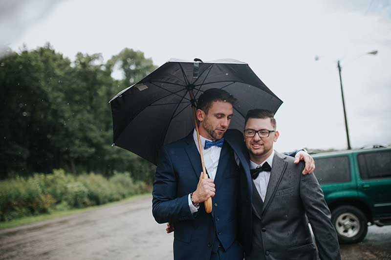 Groom and groomsman walk with umbrella after wedding