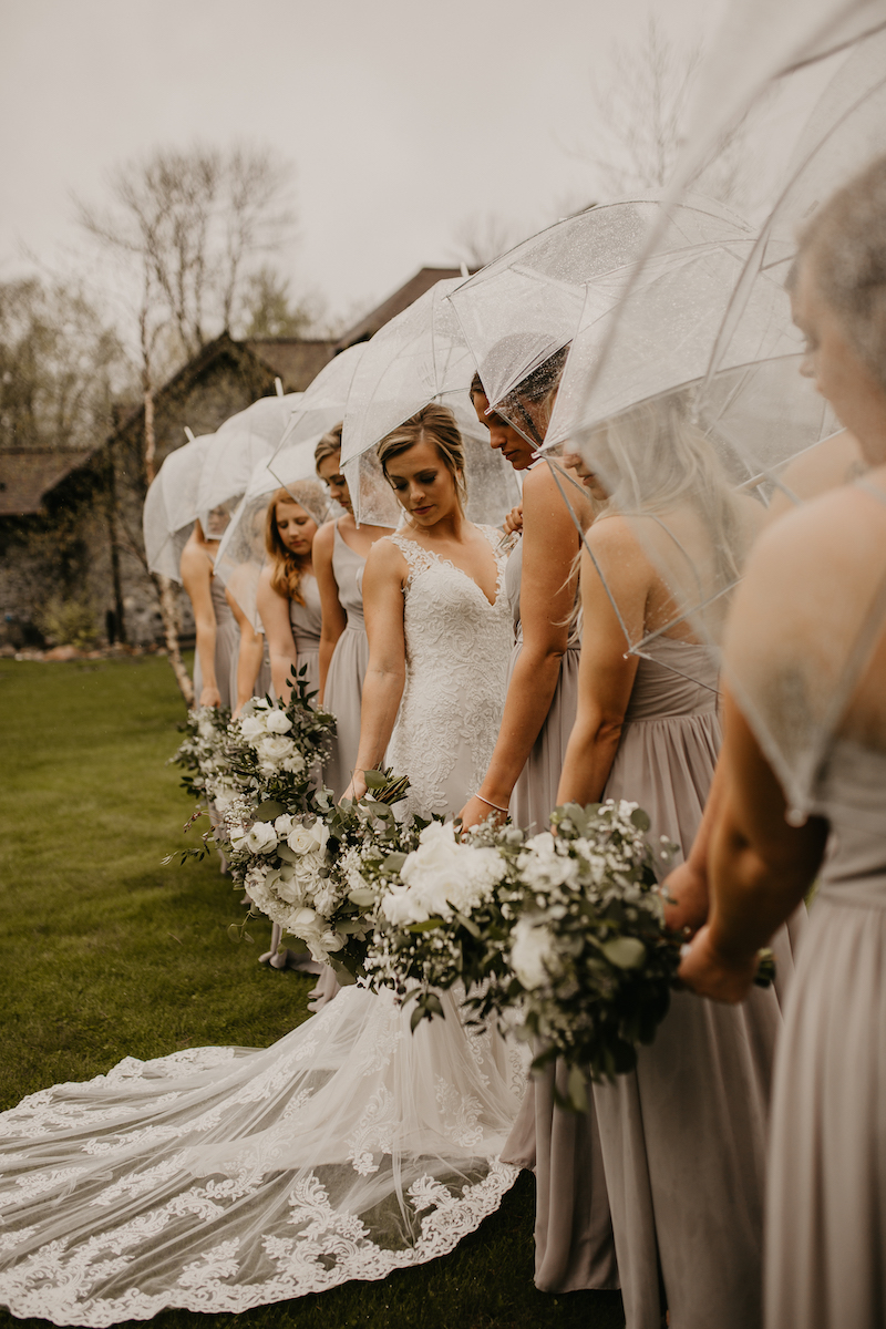 Bride and bridesmaid stand outside with clear umbrellas