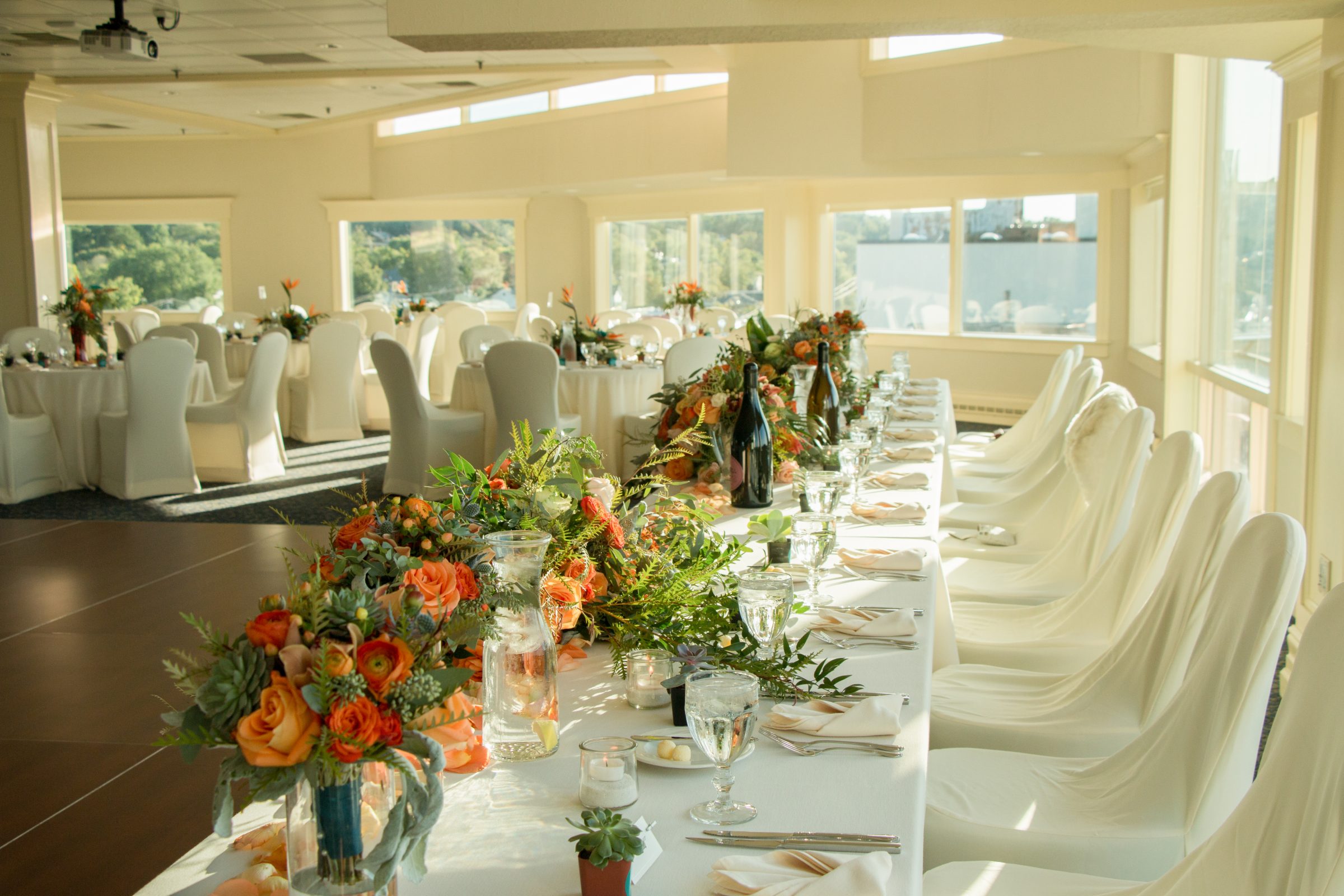 Hotel wedding reception head table white white chairs and yellow, orange, and green floral centerpieces 