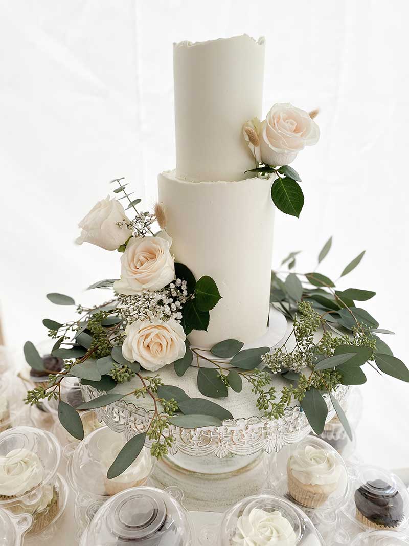 Smooth white wedding cake with greenery and roses
