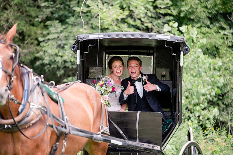 Bride and groom ride in horse drawn carriage at Sacred Clay Inn wedding