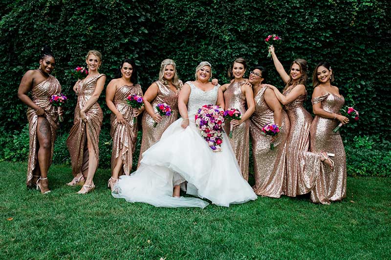 Bride in tulle ballgown poses with 8 bridesmaids in sequin rose gold gowns