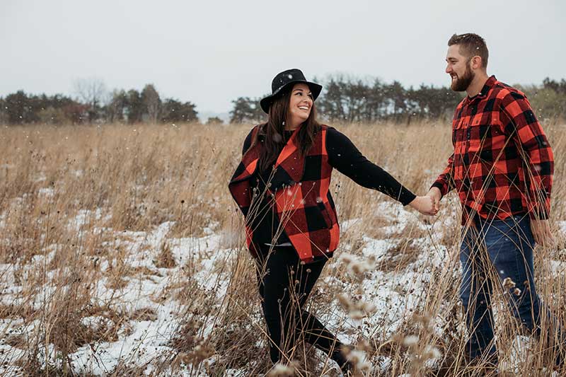 Engaged couple walks through field in red and black buffalo check tops