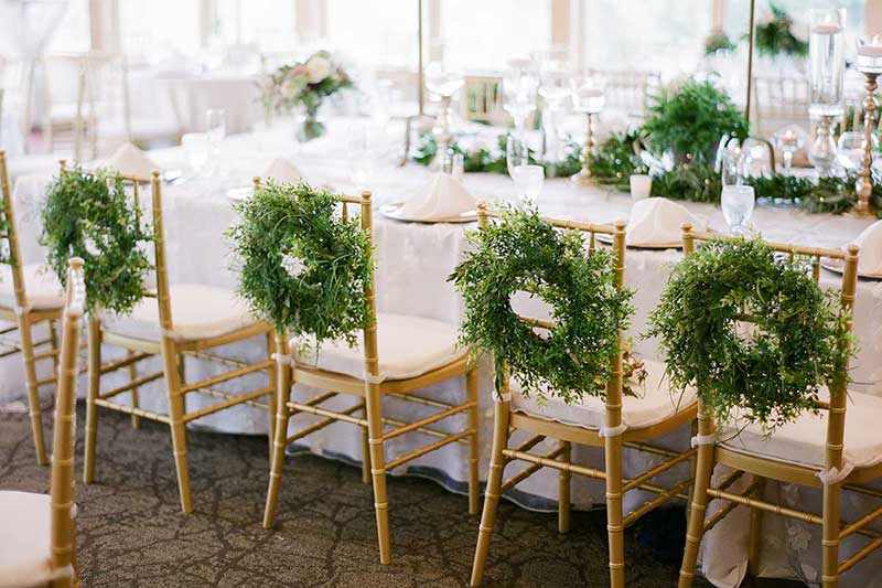 Gold chivari chairs with green wreaths hanging on back