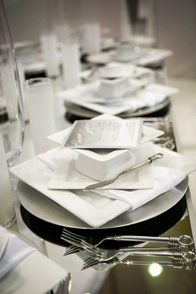 All white wedding tabletop decor with plates, silverware, napkins, and a menu at winter inspiration stations