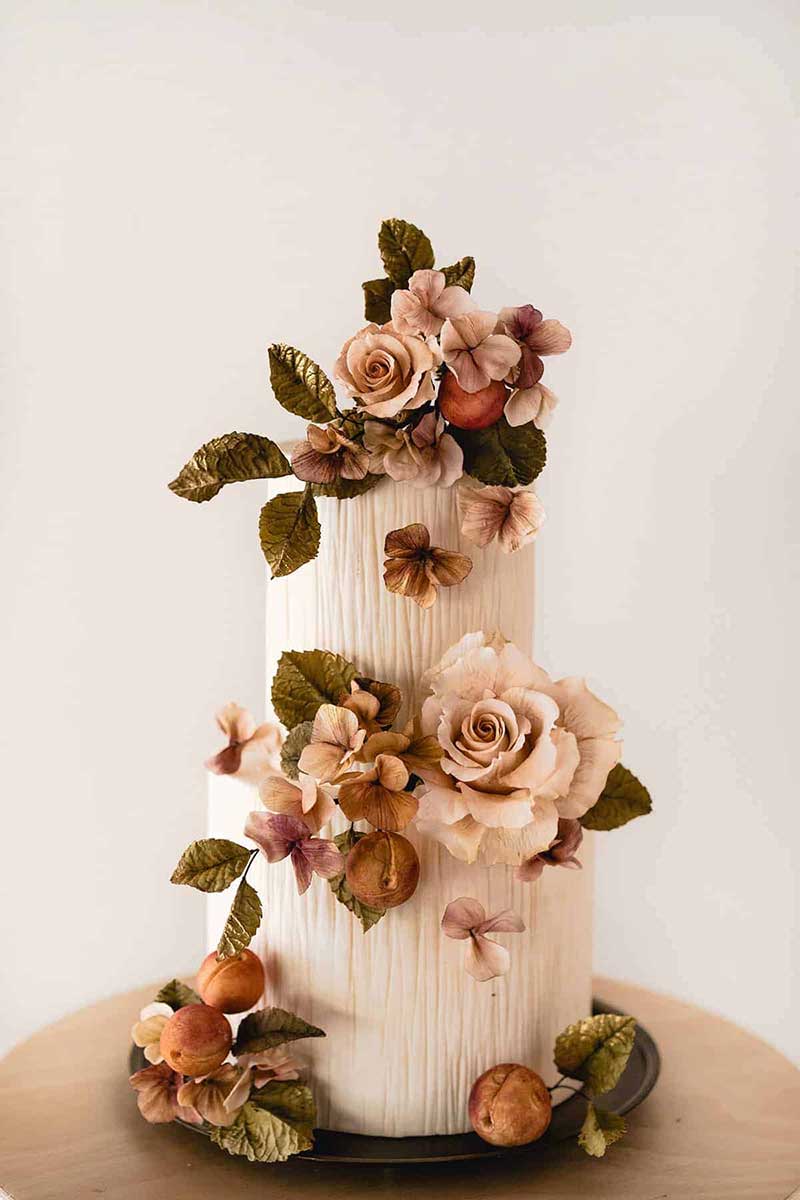 Intricate white wedding cake with dark green, orange, and blush sugar flowers