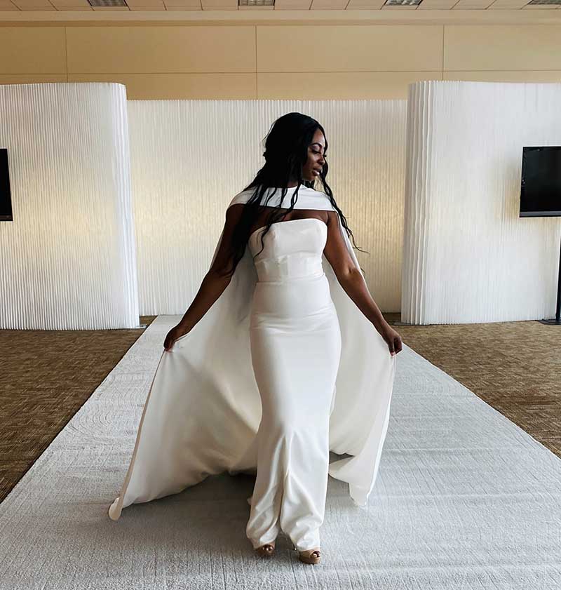 Simple crepe wedding dress with a long crepe cape on bridal fashion show runway