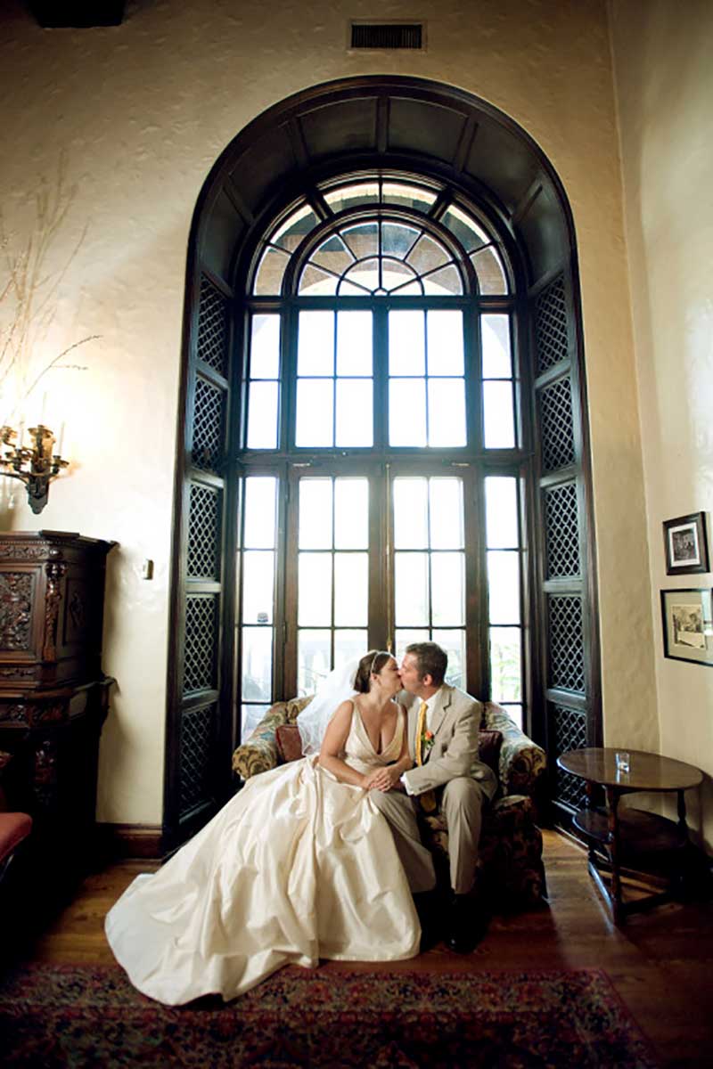 Bride and groom sit in front of floor to ceiling window 