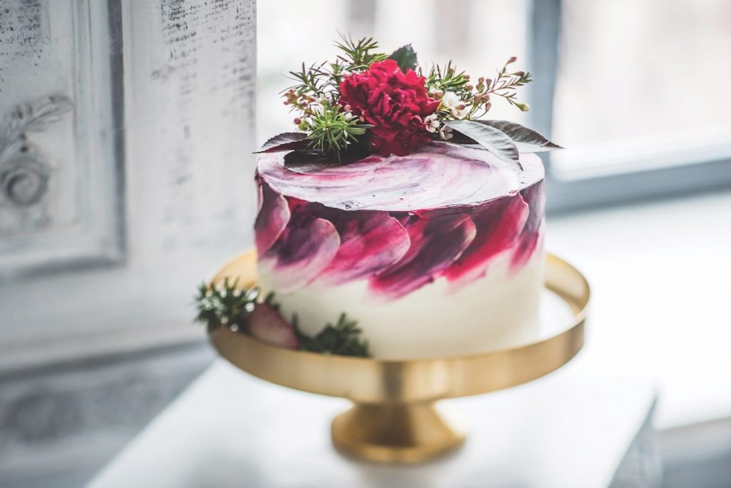Single-tier white wedding cake with purple and pink swirls with red rose and greenery atop