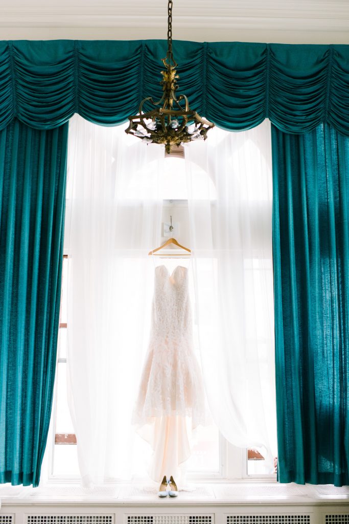 Strapless white dress hangs from window with tall teal drapes 