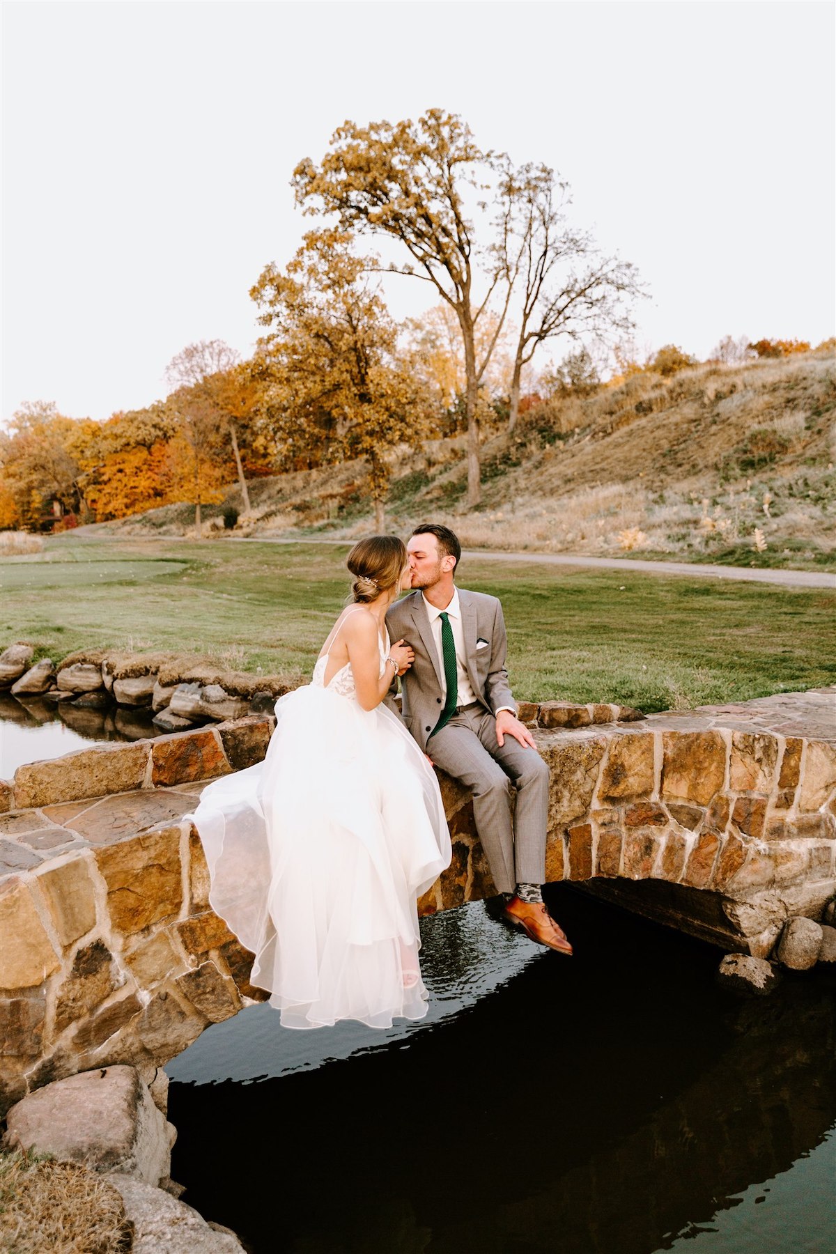 Bride and groom sit on bridge at golf course wedding at Hazeltine National Golf Club in Minnesota 