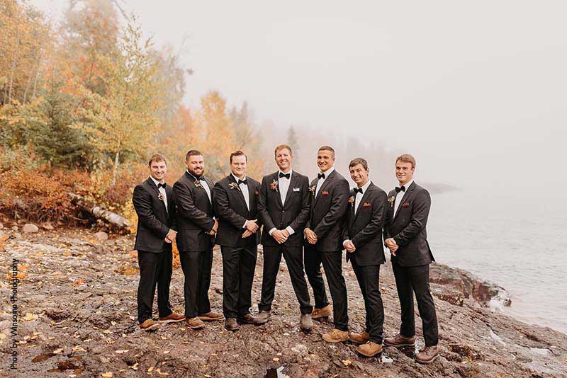 Groom stands with groomsmen in black suits