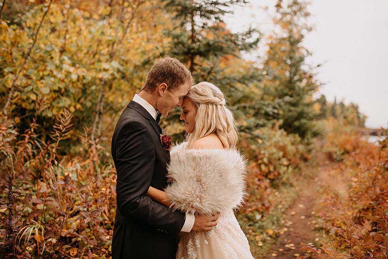 Bride and groom stand by trees with fall leaves