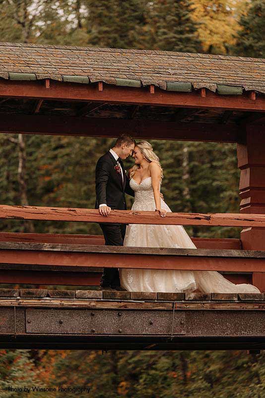 Bride and groom stand on bridge overlooking river