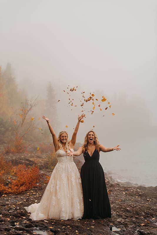 Bride and bridesmaid throw fall leaves into the air