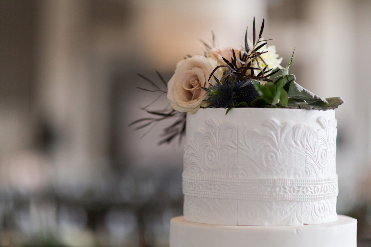 Intricate white wedding cake with floral and greenery atop