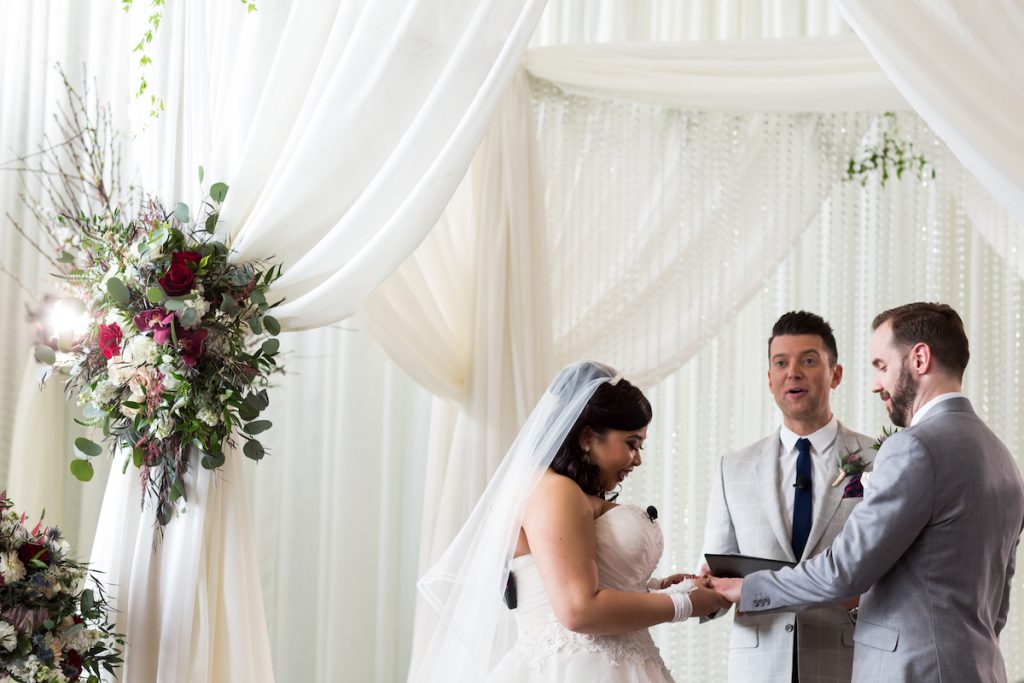 Bride and groom share vows under white draped arch