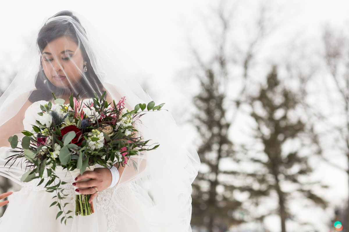 Winter bride stands outside with veil over face