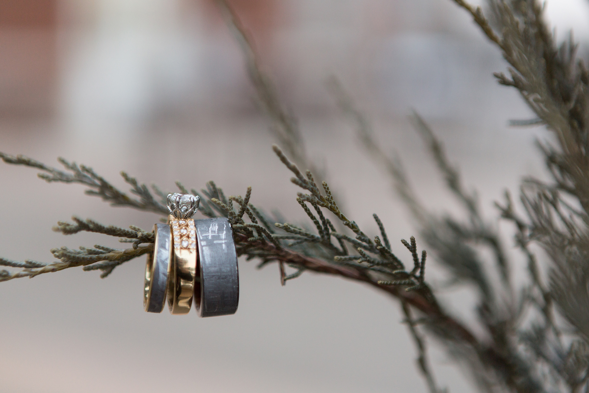 Gray wedding bands and rose gold engagement ring hang on pine tree