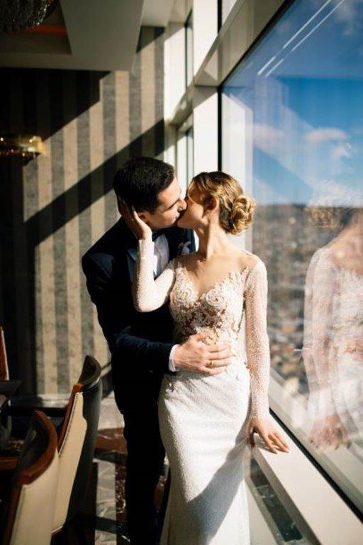 Man in custom black suit kisses bride in long-sleeve embellished bridal gosn