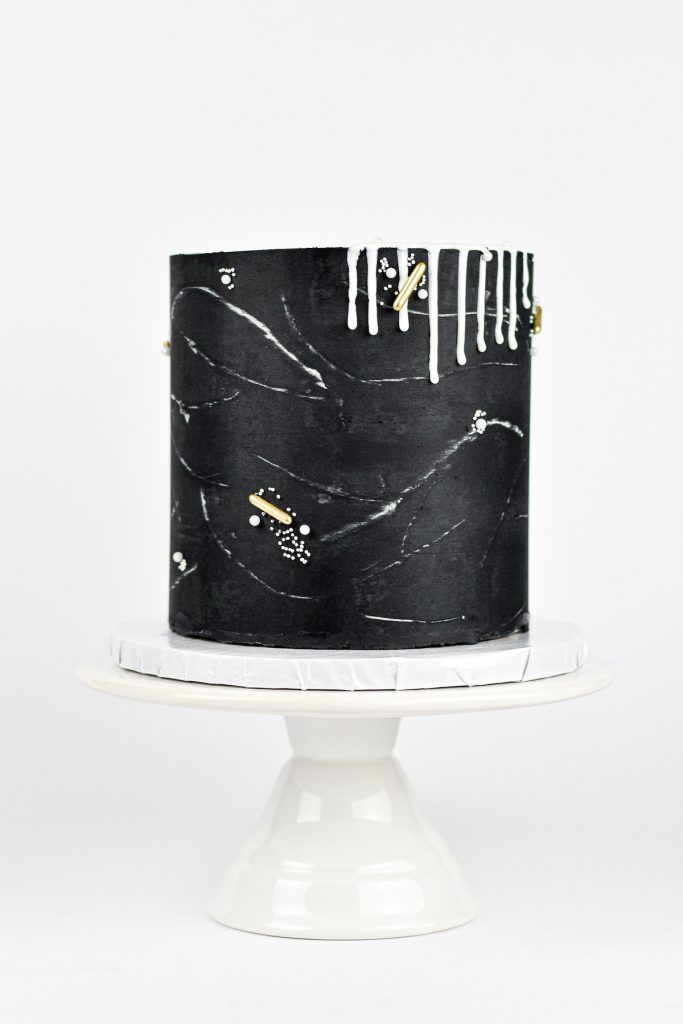 Single-tier black wedding cake with white drip and gold details 