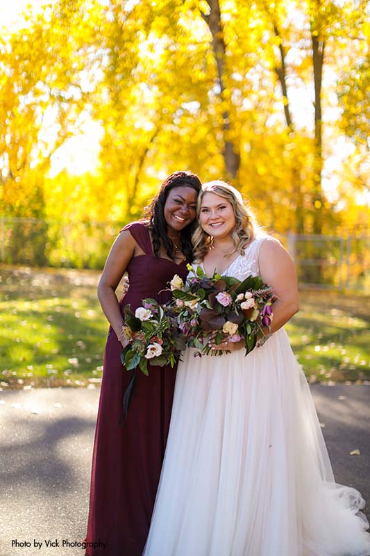 Bride in ballgown poses with bridesmaid in maroon dress