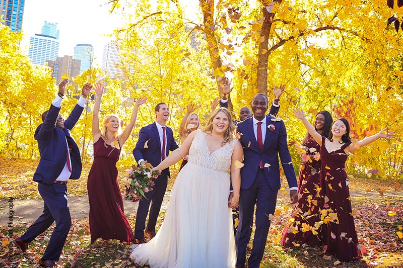 Wedding party throws leaves up in the air as they land on bride and groom