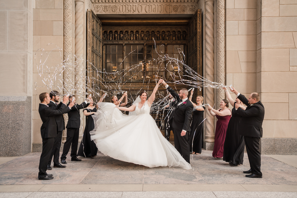 Bride in large white ball gown twirls as wedding party throws confetti