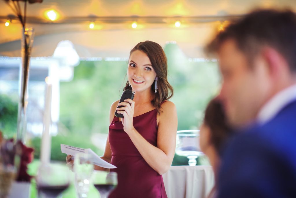 Bridesmaid in maroon gown gives a speech at a wedding